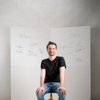 Frontalportrait, vor wei&szlig;en Wand mit Unterschriften sitzend | Copyright: Holger D&uuml;lken